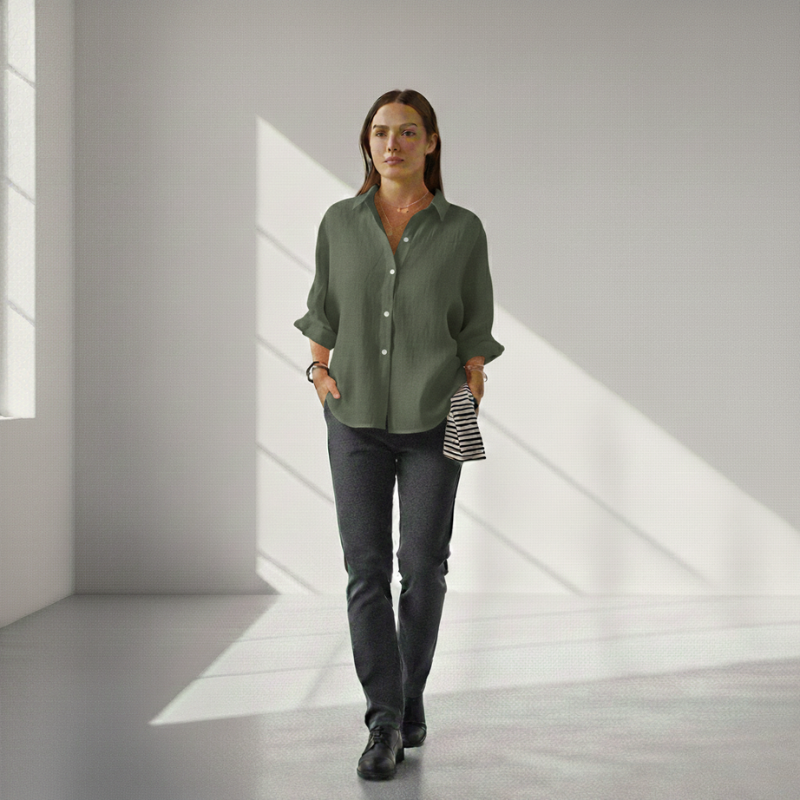 Woman wearing a green shirt and dark pants in a minimalistic room with light streaming through a window.