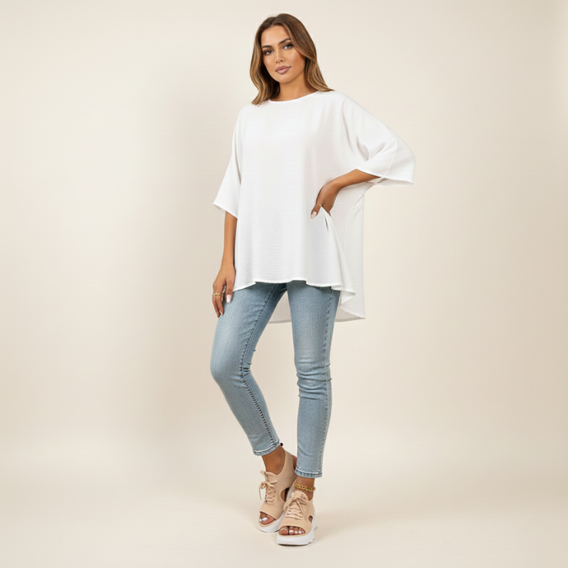 Woman wearing a white oversized shirt and light blue jeans on a plain background