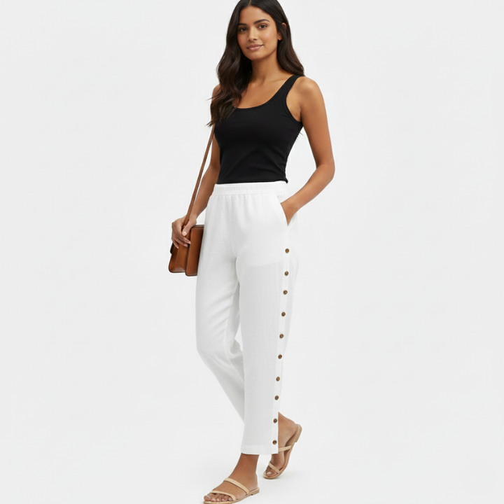 Woman wearing a black tank top and white pants with buttons on a white background