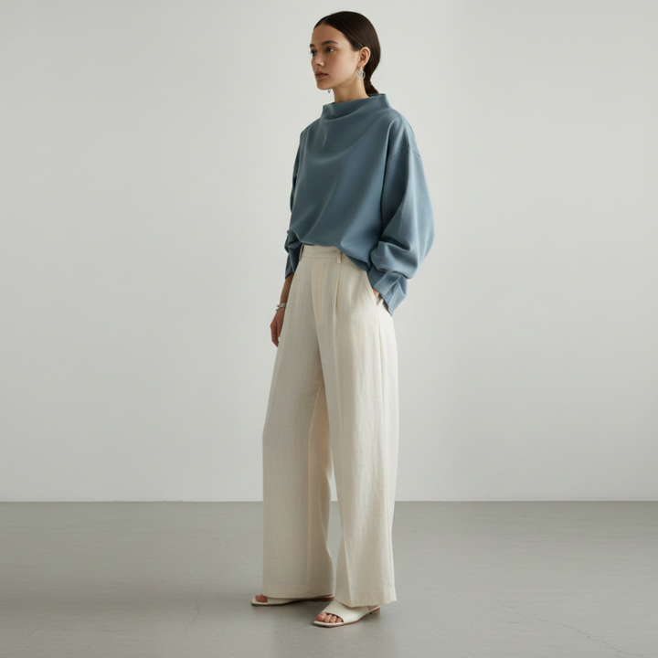 Woman wearing a blue sweater and white pants against a plain background