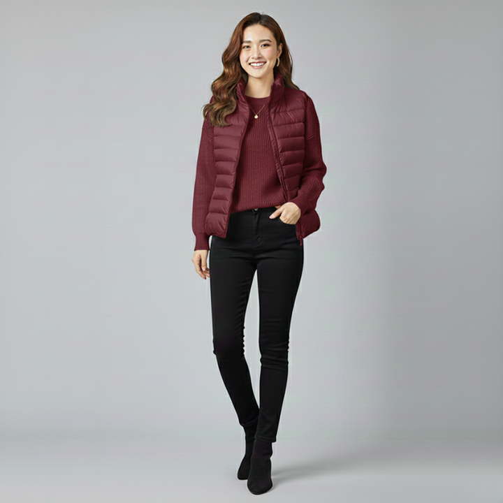 Woman wearing a maroon puffer jacket and black pants on a gray background