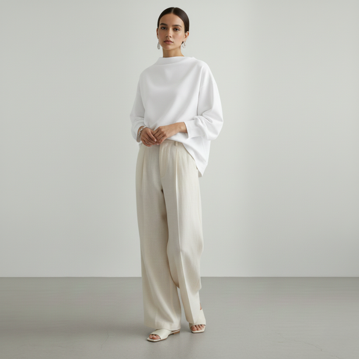 Woman wearing a white top and beige pants against a plain background