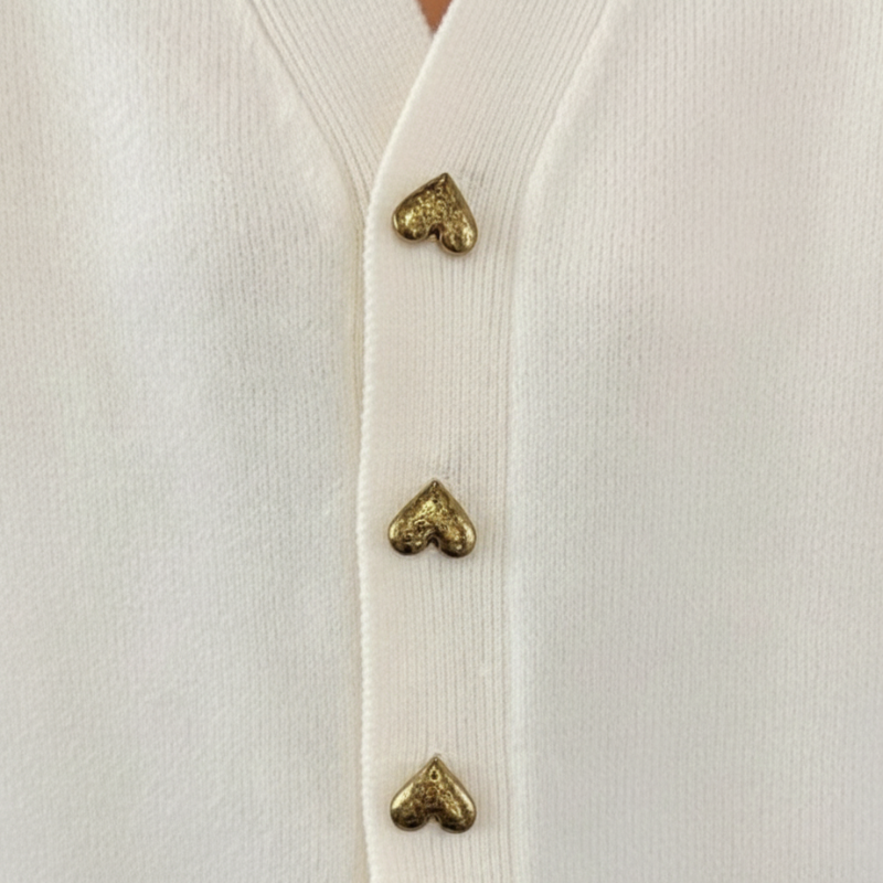 Close-up of a white cardigan with gold heart-shaped buttons.