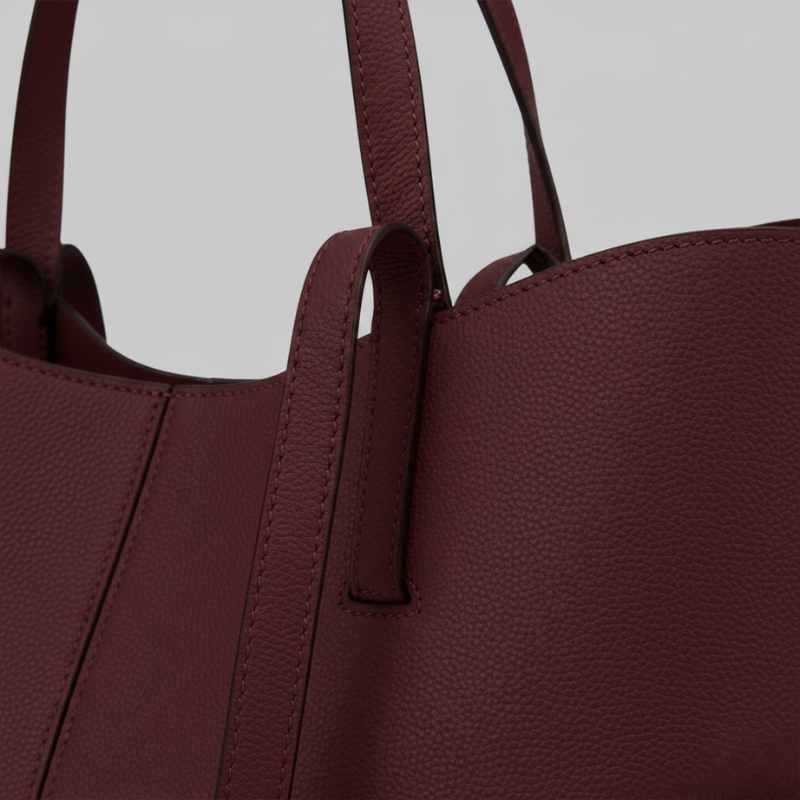 Close-up of a burgundy leather tote bag showing smooth texture and clean stitching.