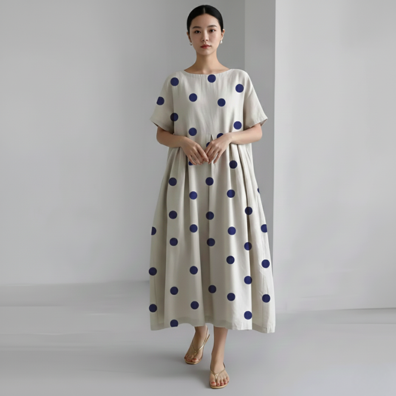 Woman wearing a long beige dress with blue polka dots against a plain background