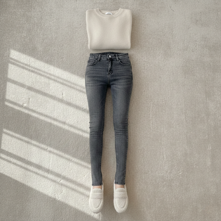 Gray jeans and white sweater displayed against a gray wall with sunlight casting shadows.