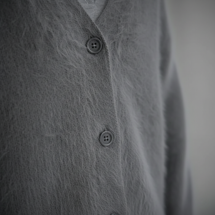 Close-up of a gray knit cardigan showing button stitching, soft textured fabric, and ribbed detailing.
