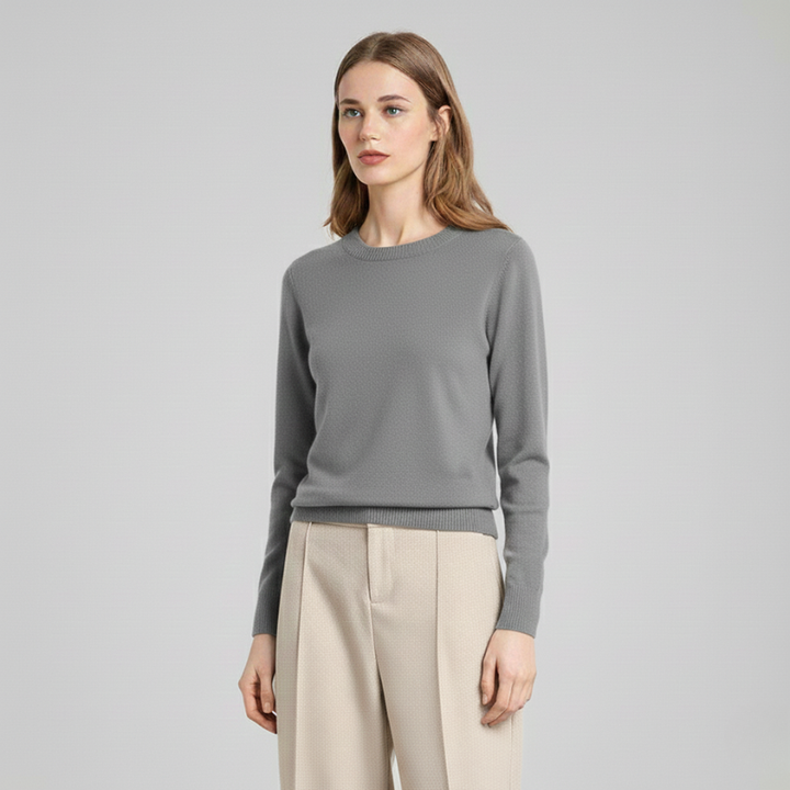 Woman wearing a light gray knit sweater in a studio, showcasing soft, everyday women’s knitwear.
