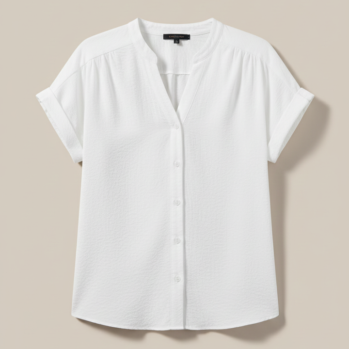 Flatlay of a white short-sleeve V-neck blouse with soft drape and minimal design displayed on a neutral background.