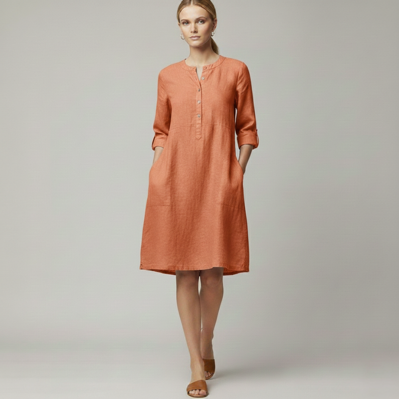Woman wearing an orange knee-length casual dress with 3/4 sleeves and a minimal buttoned neckline in natural indoor lighting.