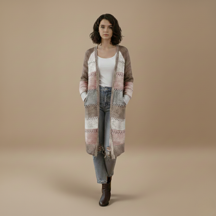 Woman walking indoors wearing a long patchwork cardigan styled casually with jeans and boots.
