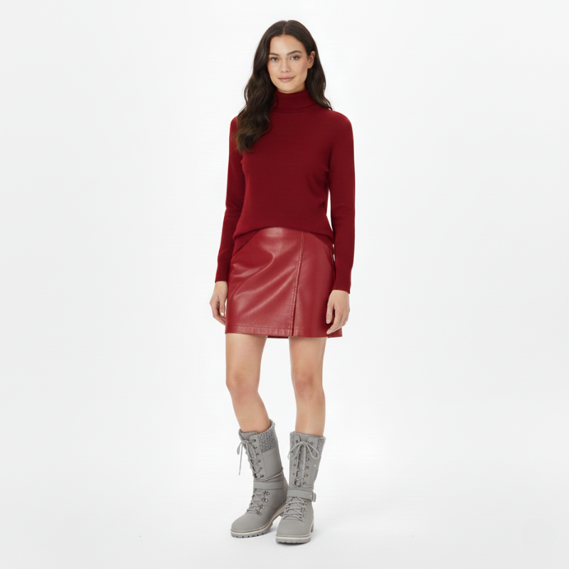 Woman wearing a red knit sweater paired with a burgundy leather mini skirt and ankle boots in a studio setting.