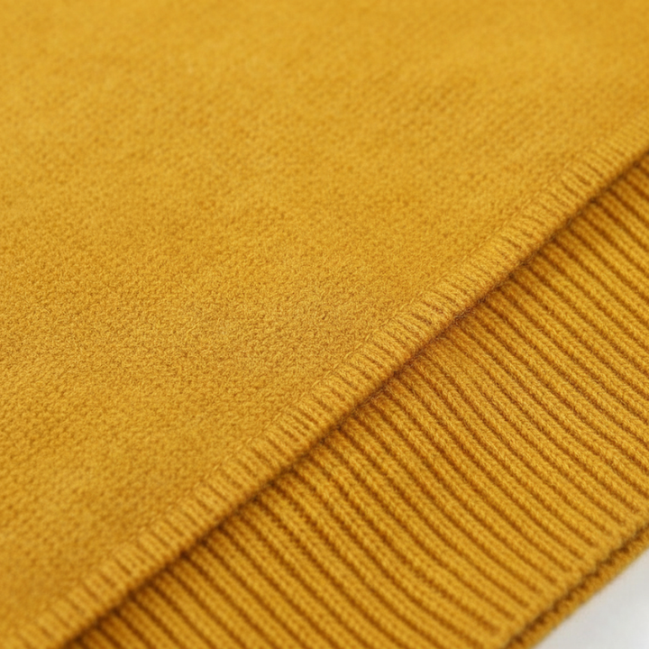 Close-up of mustard yellow knit sweater fabric showing ribbed texture and stitching details.