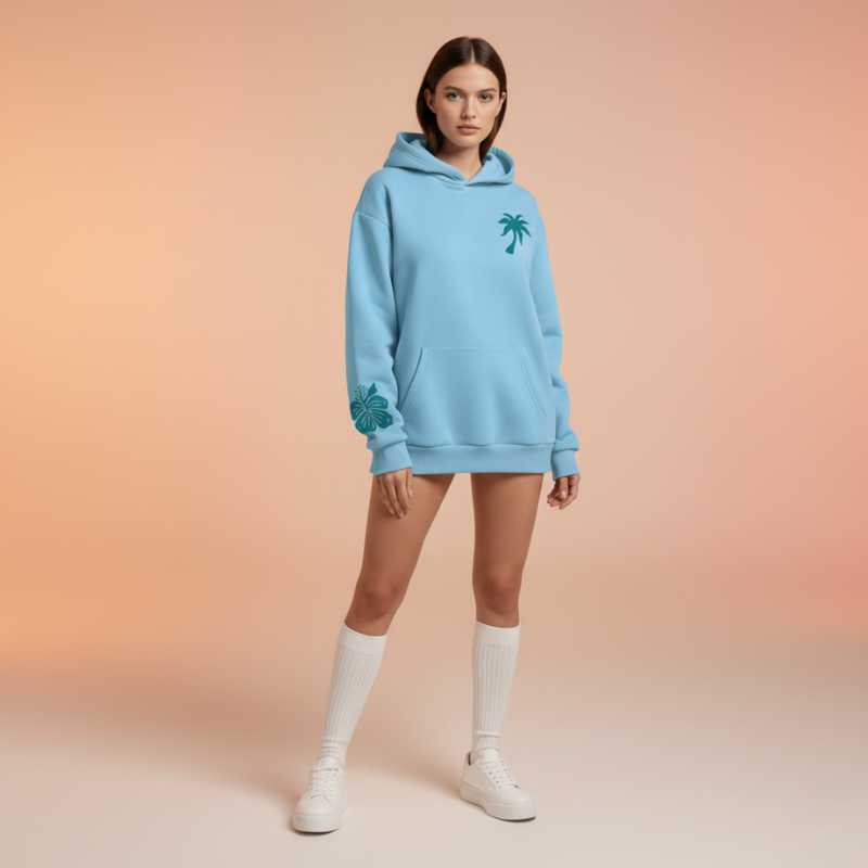 Woman wearing a light blue hoodie with a palm tree design on a gradient background